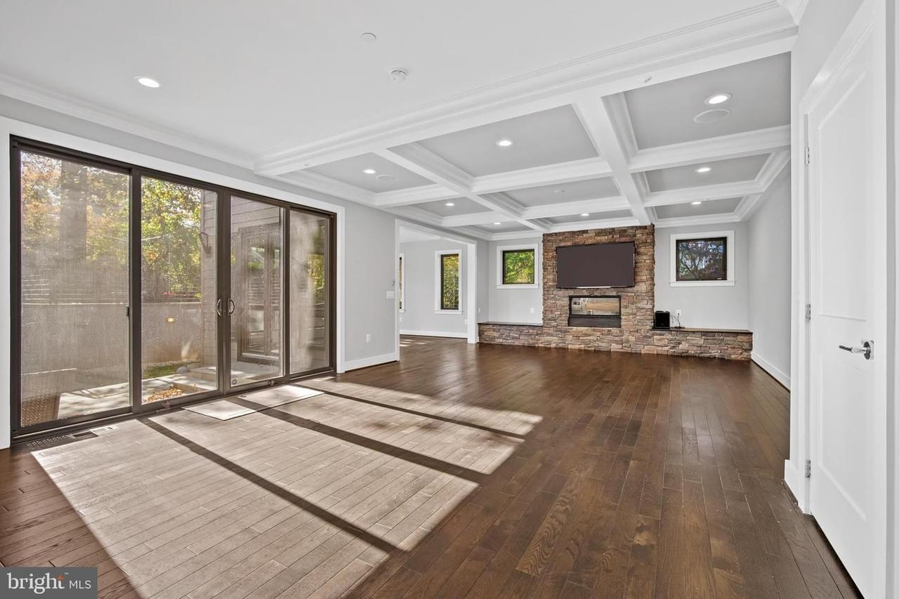 A large, open living room with light gray walls, huge glass french doors, large focal fireplace with stone facade, architectural detailing on the ceiling